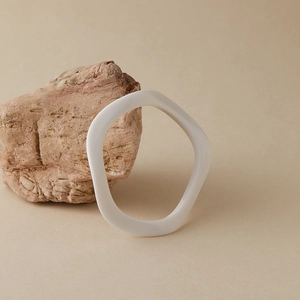 Détail du bracelet en acrylique blanc ondulé posé sur une pierre beige naturelle