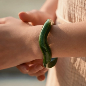 Bracciale minimalista in acrilico verde scuro a forma di onda indossato su un polso