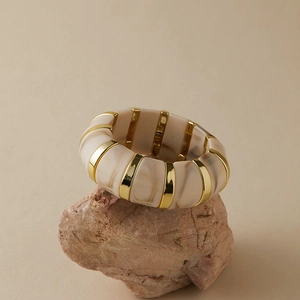 Détail du bracelet en résine marbrée beige avec bandes dorées sur support en pierre