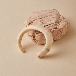Primo piano del bracciale aperto in acrilico crema con venature marroni su pietra naturale
