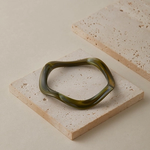 Détail d'un bracelet acrylique ondulé avec des textures marbrées vert olive et ambre