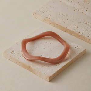 Détail d'un bracelet acrylique rose à vagues sur des pierres en travertin minimalistes