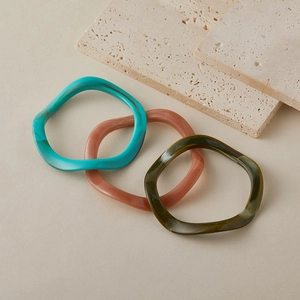 Détail de trois bracelets ondulés en acrylique aux textures marbrées turquoise, rose et olive