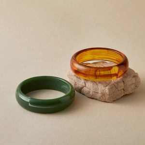 Bohemian acrylic bangles in amber orange and deep green colors on a natural stone