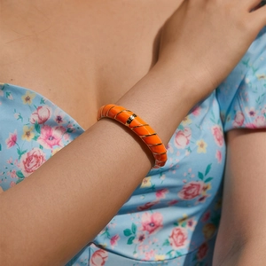 Dettaglio del bracciale smaltato arancione con linee dorate su manica a fiori
