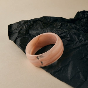 Gros plan d'un large bracelet en acrylique avec texture marbre rose orangé sur papier noir