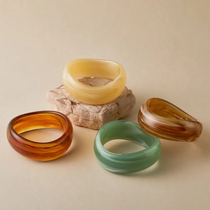 Detailed view of four chunky acrylic bangles with amber and marble texture on stone