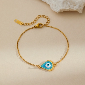 Detail of gold evil eye bracelet with lobster clasp on beige background with stone