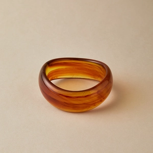 Macro view of amber acrylic bangle with reddish-brown marble texture and smooth edges