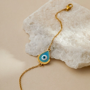 Detail of gold evil eye bracelet with blue enamel charm on white natural stone