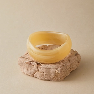 Close-up of amber marble pattern acrylic bangle on a textured stone display pedestal