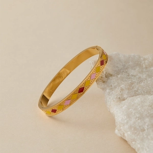 Dettaglio del bracciale dorato con smalto geometrico posato su una pietra bianca