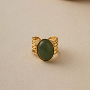 Close-up of wide gold stainless steel ring featuring a large oval green stone setting