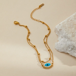 Close-up of golden double-layer chain bracelet with blue evil eye pendant and gold lashes
