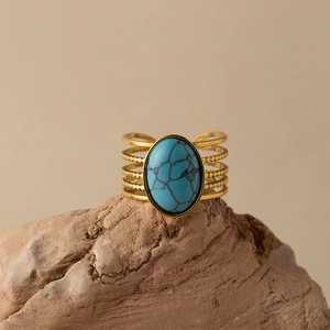 Detail of bohemian gold layered ring with a large oval turquoise on a natural stone