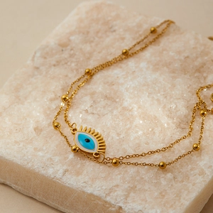 Close-up of gold double-layer evil eye bracelet with enamel pendant on mineral stone