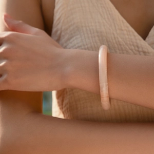 Détail d'un bracelet en résine rose pâle avec texture marbrée au poignet sous lumière douce