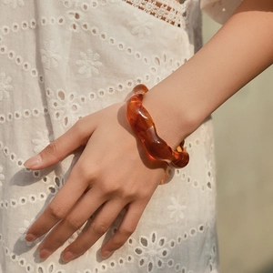 Dettaglio del bracciale in acrilico ambrato a onde indossato sul polso con ricamo
