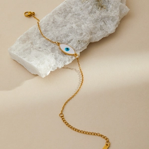 Detail of gold evil eye bracelet with white enamel charm on a natural crystal stone