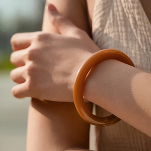 Dettaglio del bracciale in acrilico ambrato con design a onde e finitura lucida a specchio