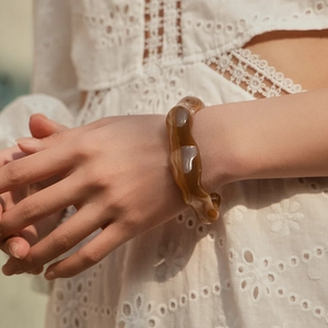 Dettaglio macro del bracciale in acrilico marrone ambra con trame e motivi a onde irregolari