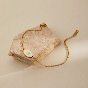 Detail of golden Hamsa Hand bracelet with blue evil eye charm on a textured stone surface