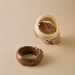 Detail view of thick marble pattern and beige acrylic bracelets on a stone prop
