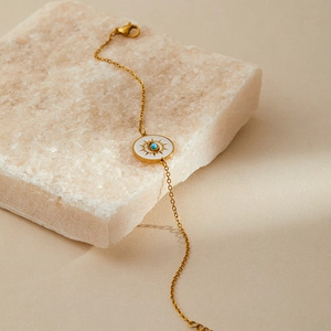 Detail of gold evil eye bracelet with white enamel and turquoise on white stone