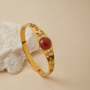 Dettaglio di bracciale rigido dorato vintage con gemma rossa e motivi a forma di occhio