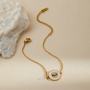 Detailed macro view of gold evil eye pendant on a thin stainless steel chain bracelet