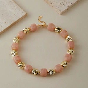 Dettaglio di perle in resina marmorizzata rosa e accenti metallici dorati su collana