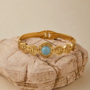 Dettaglio di un bracciale dorato con motivi a occhio bohémien e pietra turchese