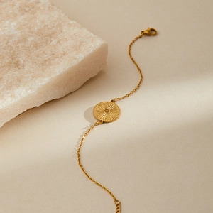 Detailed shot of golden stainless steel bracelet with sunburst pendant and lobster clasp