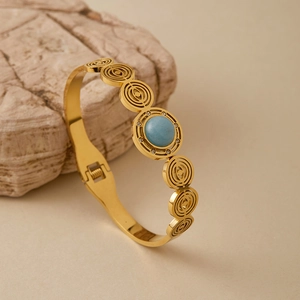 Dettaglio di un bracciale dorato geometrico con gemma blu e zirconi incastonati