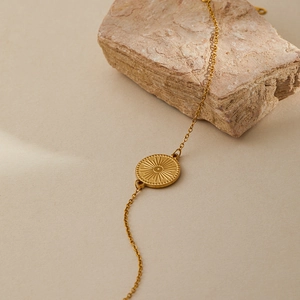 Detailed view of a gold-plated stainless steel bracelet with a radial sun pendant