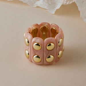 Détail du bracelet en résine marbrée rose avec rivets dorés et bande élastique