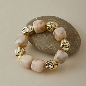 Bracelet élastique en cubes de résine marbre beige et perles en métal doré sur une pierre