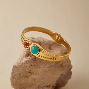 Dettaglio del bracciale in acciaio dorato con turchese e pietra rossa su roccia