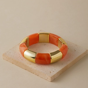 Detail of chunky orange marble resin and gold metal segmented stretch bracelet on stone