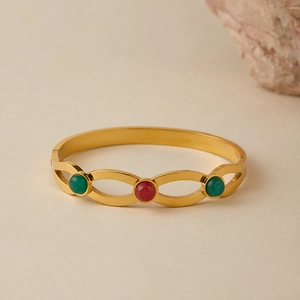 Dettaglio del bracciale rigido dorato con intarsi di pietre rosse e verdi