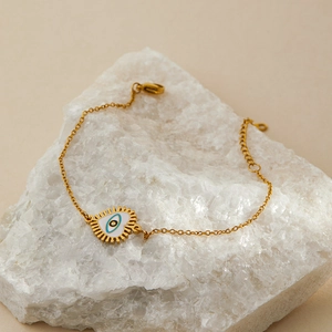 Detail of gold-plated evil eye heart bracelet with white enamel on crystal rock