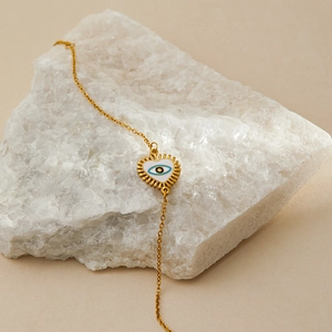 Detailed shot of golden Evil Eye heart pendant with white enamel on crystal rock