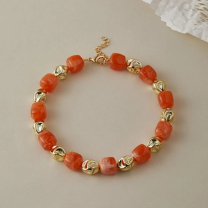 Dettaglio di perle in resina arancione marmorizzato e perle in metallo dorato