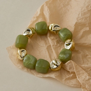 Gros plan de perles en résine vert olive et métal doré texturé sur papier kraft