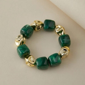 Détail macro des perles en résine vert foncé et des perles en métal doré sur le bracelet