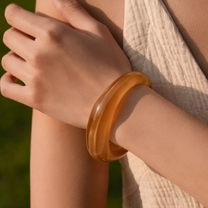 Primo piano di un bracciale rigido in resina ambrata su tessuto sotto la luce naturale