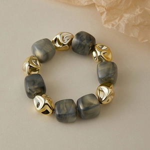 Bracelet élastique avec perles dorées métalliques et carrés en résine marbrée sur fond beige