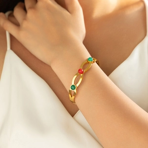 Elegante bracciale rigido dorato a onde con pietre preziose verdi e rosse al polso