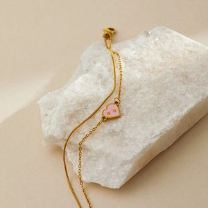 Detail of gold double-layer chain bracelet featuring a pink heart pendant on white crystals