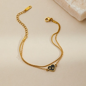 Detail of gold double-layer bracelet with black heart charm and snake chain texture